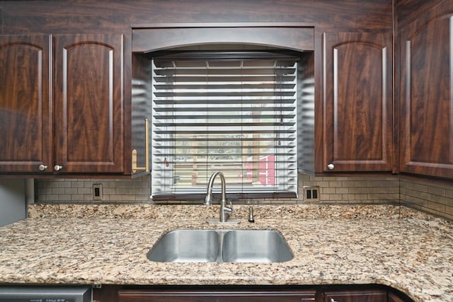 kitchen with backsplash, light stone counters, dark brown cabinets, sink, and dishwasher