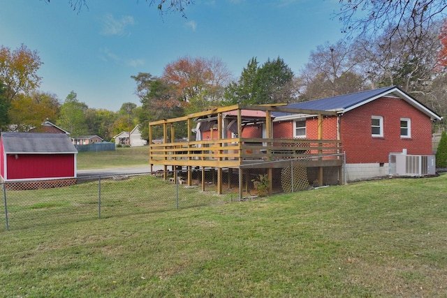 rear view of property featuring a lawn, a wooden deck, a storage unit, and central AC