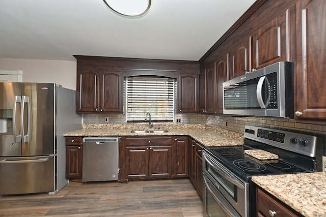 kitchen featuring dark wood-type flooring, sink, appliances with stainless steel finishes, light stone counters, and dark brown cabinetry