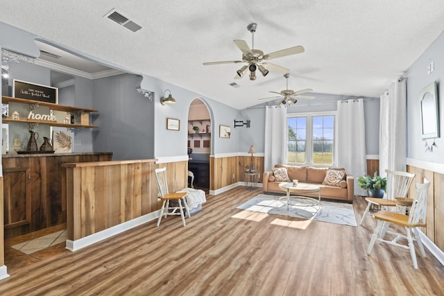 living room featuring a textured ceiling, vaulted ceiling, ceiling fan, wood-type flooring, and wood walls