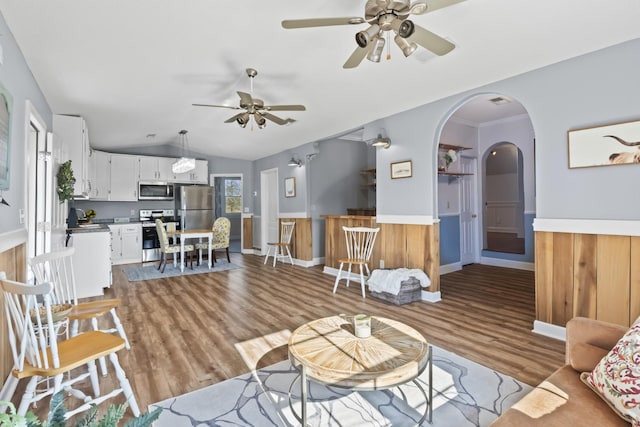 living room with ceiling fan, wooden walls, lofted ceiling, and light wood-type flooring