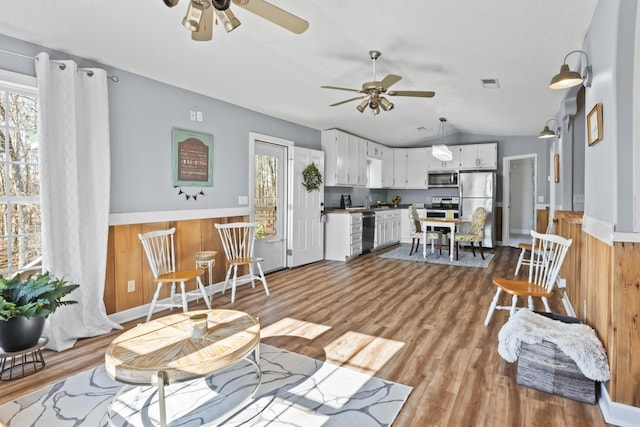 living room with light wood-type flooring, vaulted ceiling, ceiling fan, and wooden walls