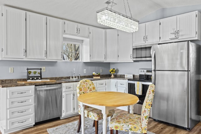 kitchen featuring sink, stainless steel appliances, an inviting chandelier, lofted ceiling, and white cabinets