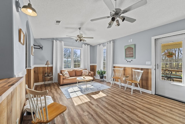 living room with lofted ceiling, wood walls, wood-type flooring, and a textured ceiling