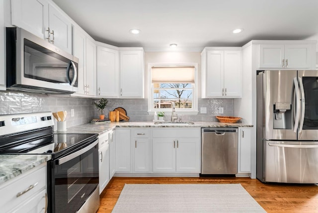 kitchen with light stone countertops, stainless steel appliances, sink, light hardwood / wood-style floors, and white cabinetry