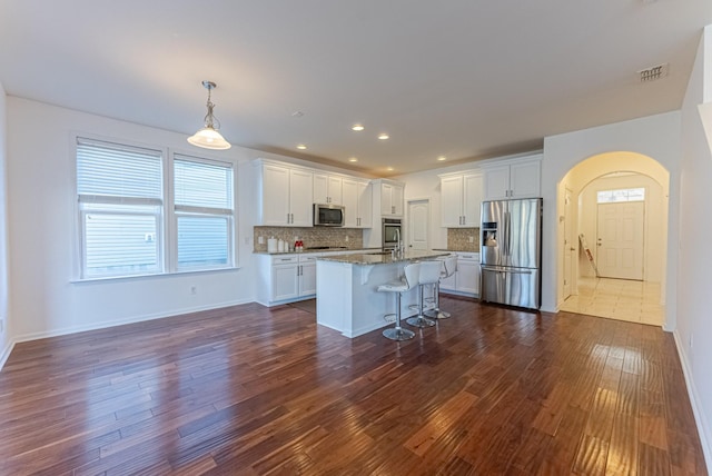 kitchen featuring a breakfast bar, a center island with sink, white cabinets, decorative backsplash, and appliances with stainless steel finishes