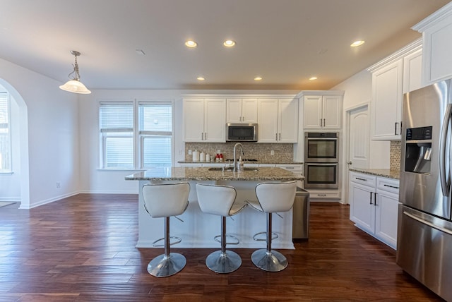 kitchen with appliances with stainless steel finishes, backsplash, a center island with sink, white cabinetry, and hanging light fixtures