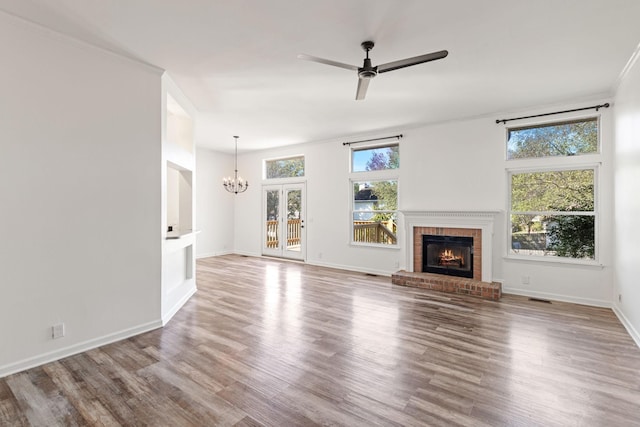 unfurnished living room with french doors, ceiling fan with notable chandelier, light hardwood / wood-style flooring, a brick fireplace, and ornamental molding