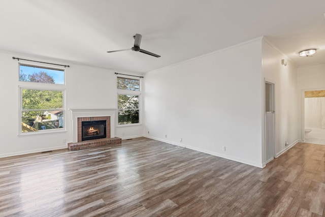 unfurnished living room with a wealth of natural light, hardwood / wood-style flooring, ceiling fan, and a brick fireplace