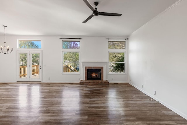 unfurnished living room with ceiling fan with notable chandelier, dark hardwood / wood-style floors, ornamental molding, and a brick fireplace