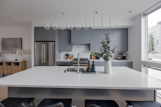 kitchen featuring a kitchen island with sink, backsplash, a kitchen breakfast bar, gray cabinets, and appliances with stainless steel finishes