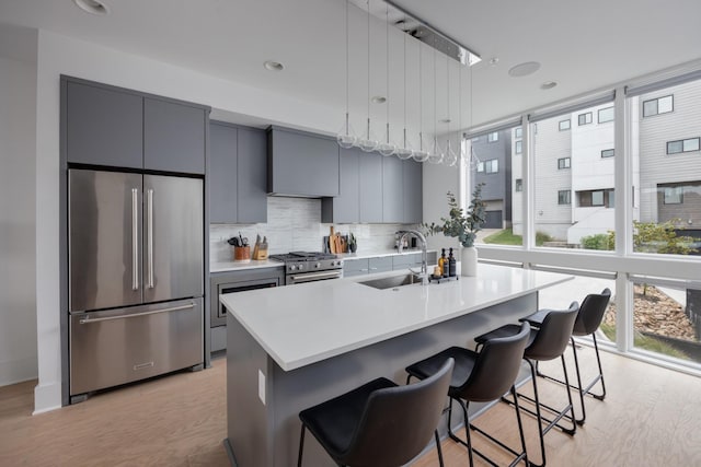 kitchen featuring gray cabinetry, sink, an island with sink, a kitchen bar, and high end appliances