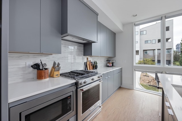 kitchen with custom exhaust hood, light hardwood / wood-style flooring, gray cabinets, tasteful backsplash, and stainless steel appliances