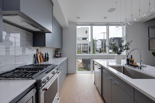 kitchen with appliances with stainless steel finishes, backsplash, wall chimney exhaust hood, gray cabinetry, and sink