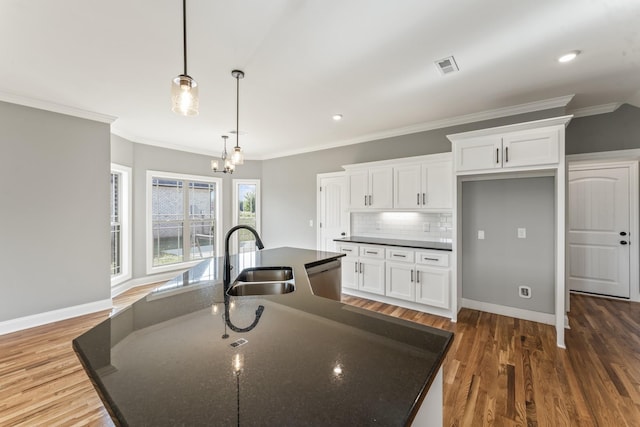 kitchen with white cabinets, sink, hanging light fixtures, and an island with sink