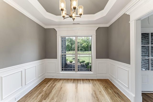 spare room with a notable chandelier, a raised ceiling, ornamental molding, and light hardwood / wood-style flooring