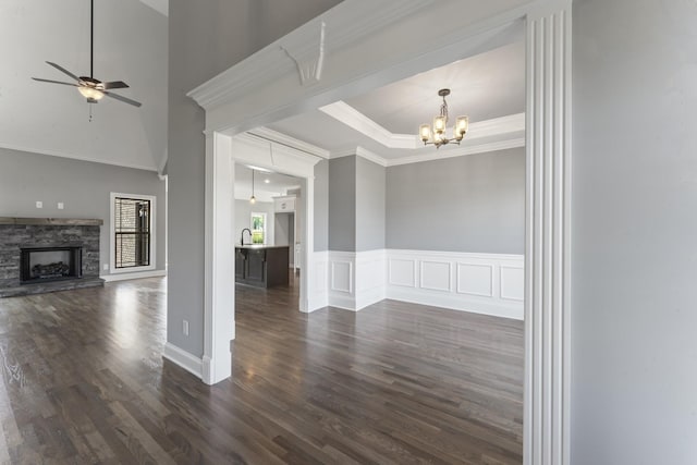 unfurnished living room featuring ornamental molding, ceiling fan with notable chandelier, dark wood-type flooring, sink, and a fireplace