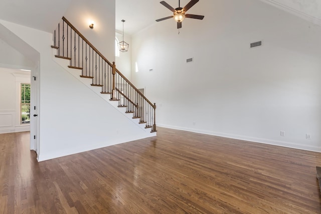 unfurnished living room featuring dark hardwood / wood-style floors, a towering ceiling, and ceiling fan with notable chandelier