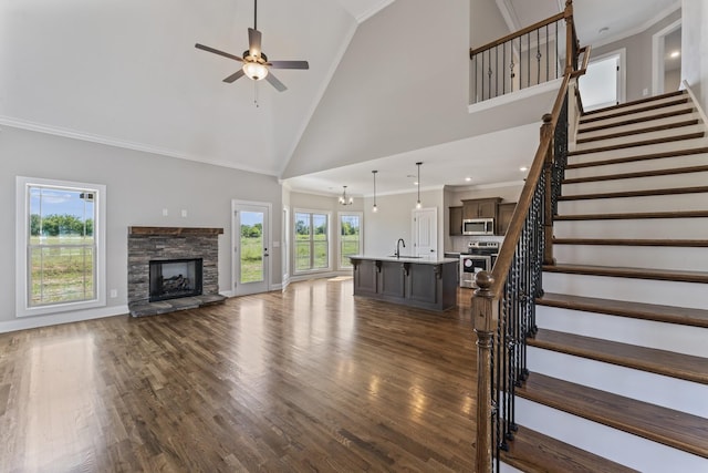 unfurnished living room with sink, high vaulted ceiling, a fireplace, ceiling fan with notable chandelier, and ornamental molding