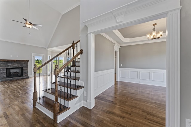 stairway with ceiling fan with notable chandelier, vaulted ceiling, crown molding, a fireplace, and hardwood / wood-style floors