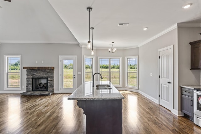 kitchen featuring light stone countertops, dark brown cabinetry, a kitchen island with sink, sink, and pendant lighting