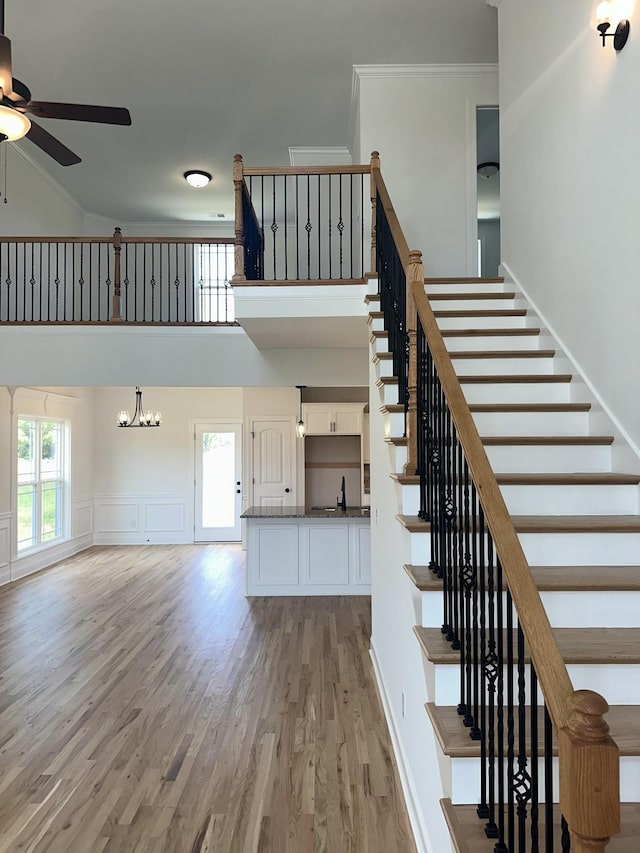 stairway featuring crown molding, wood-type flooring, and ceiling fan with notable chandelier