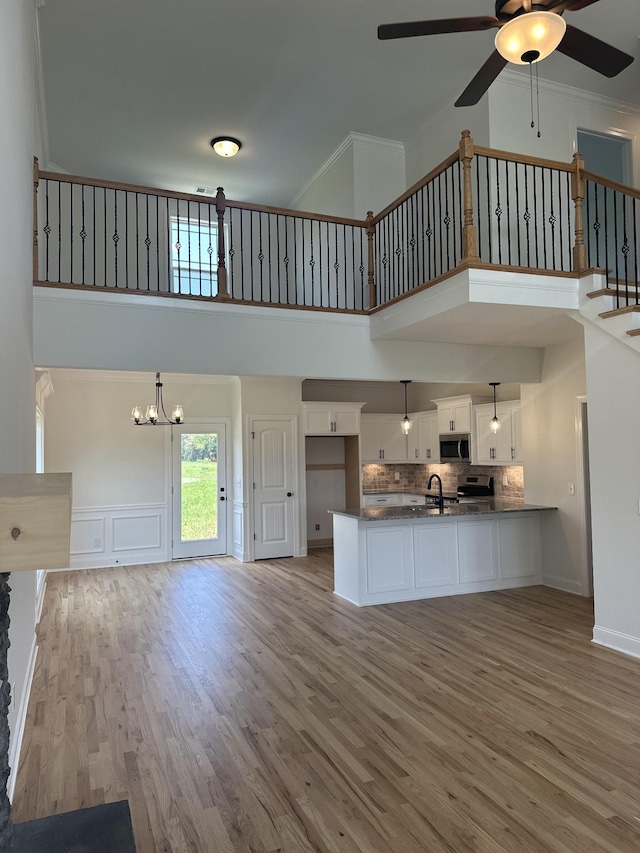 unfurnished living room featuring a towering ceiling, ornamental molding, ceiling fan with notable chandelier, sink, and light hardwood / wood-style floors