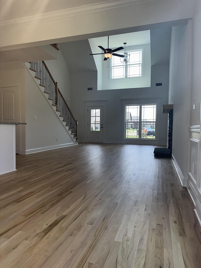 unfurnished living room with a high ceiling, hardwood / wood-style flooring, ceiling fan, and a healthy amount of sunlight