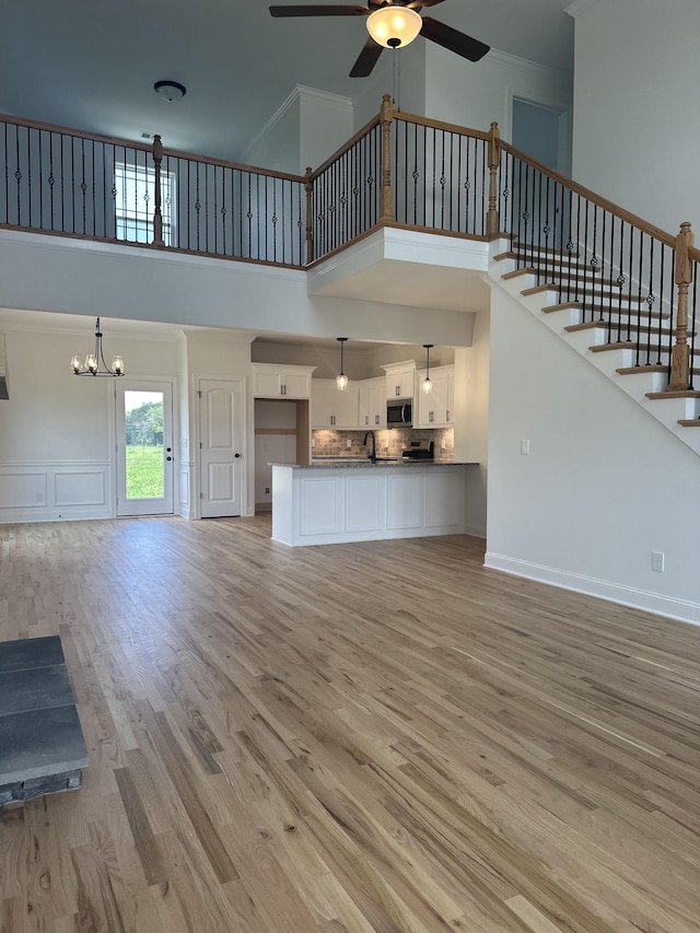 unfurnished living room with ceiling fan with notable chandelier, wood-type flooring, crown molding, and a towering ceiling