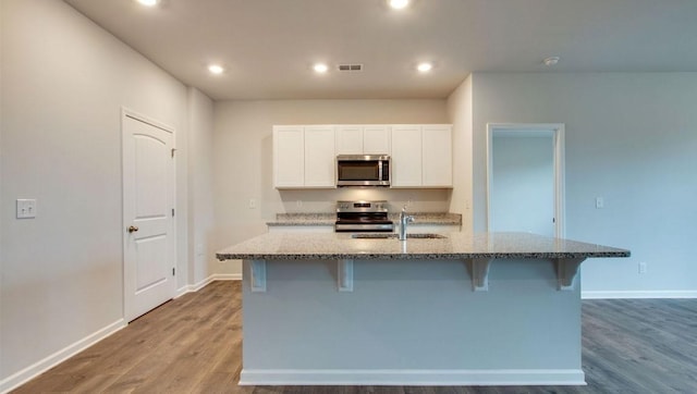 kitchen with light stone countertops, stainless steel appliances, a kitchen island with sink, sink, and white cabinetry