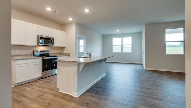 kitchen featuring white cabinets, hardwood / wood-style floors, stainless steel appliances, and a center island with sink