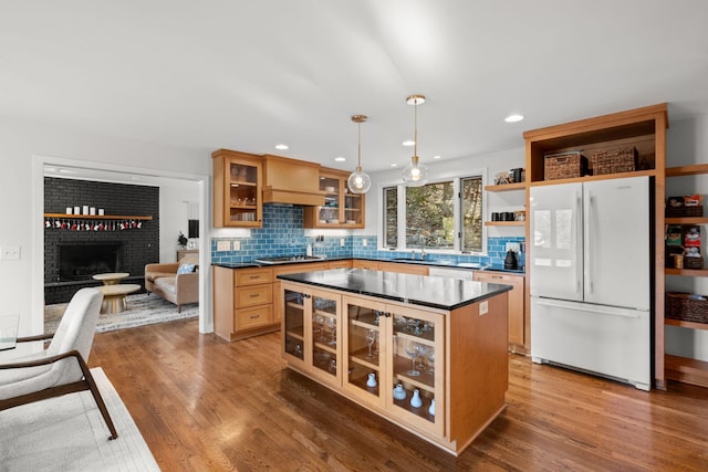 kitchen with sink, hanging light fixtures, a brick fireplace, white appliances, and hardwood / wood-style flooring