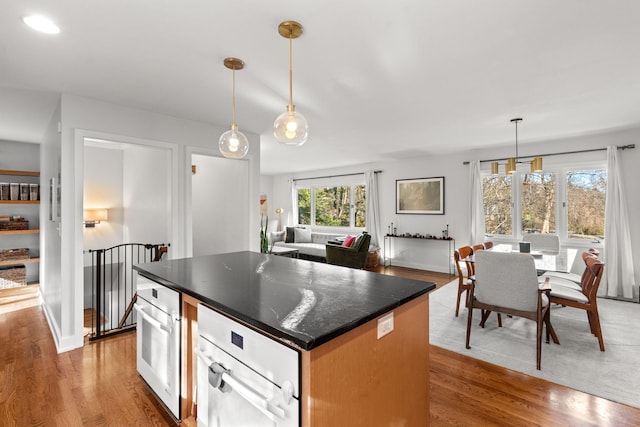 kitchen featuring light wood-type flooring, wall oven, a kitchen island, and hanging light fixtures