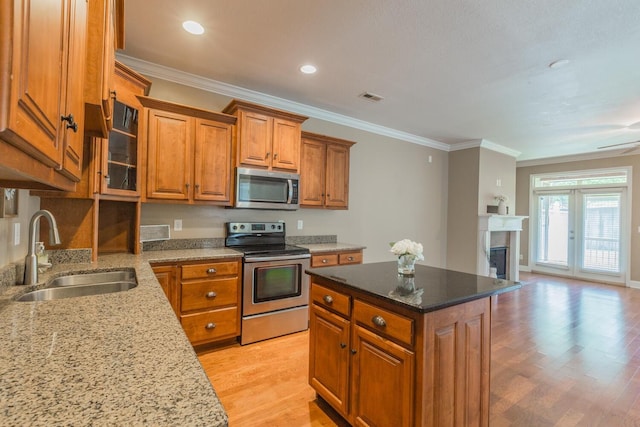 kitchen with a center island, crown molding, sink, light stone countertops, and appliances with stainless steel finishes