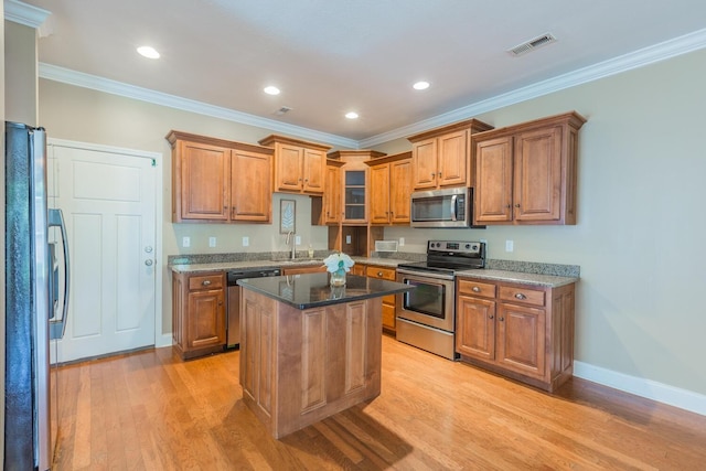 kitchen with appliances with stainless steel finishes, dark stone counters, a kitchen island, and ornamental molding