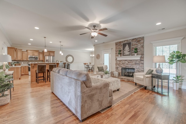 living room featuring ceiling fan, light wood-type flooring, ornamental molding, and a fireplace