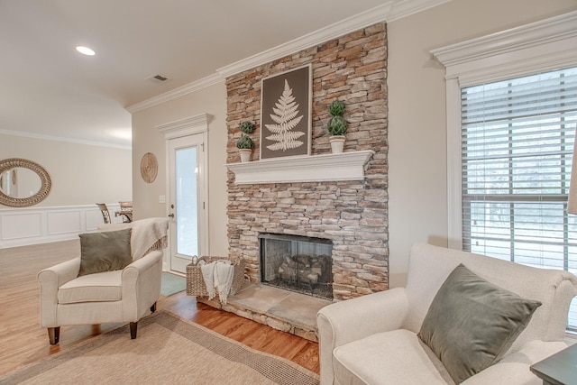 living area featuring wood-type flooring, a stone fireplace, and ornamental molding