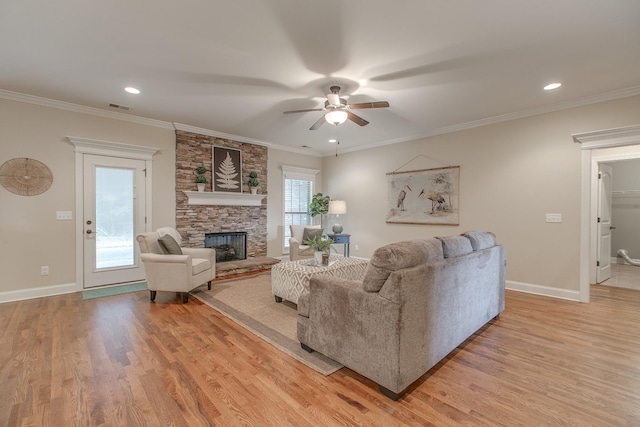 living room with a stone fireplace, ceiling fan, and ornamental molding