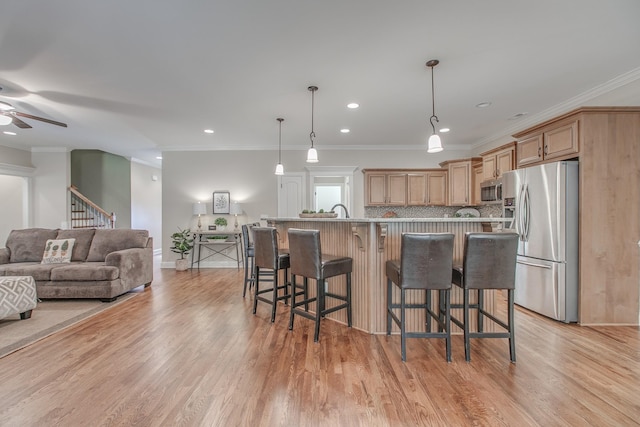 kitchen with light wood-type flooring, ornamental molding, a breakfast bar, stainless steel appliances, and hanging light fixtures