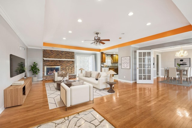 living room featuring ceiling fan with notable chandelier, ornamental molding, a fireplace, and light hardwood / wood-style flooring