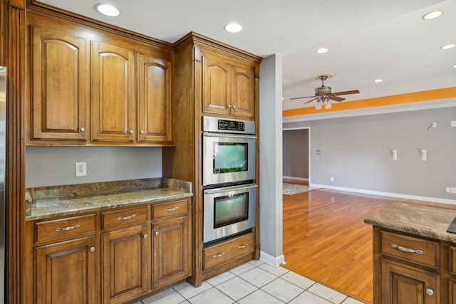 kitchen featuring ceiling fan, light tile patterned flooring, stainless steel double oven, and stone countertops