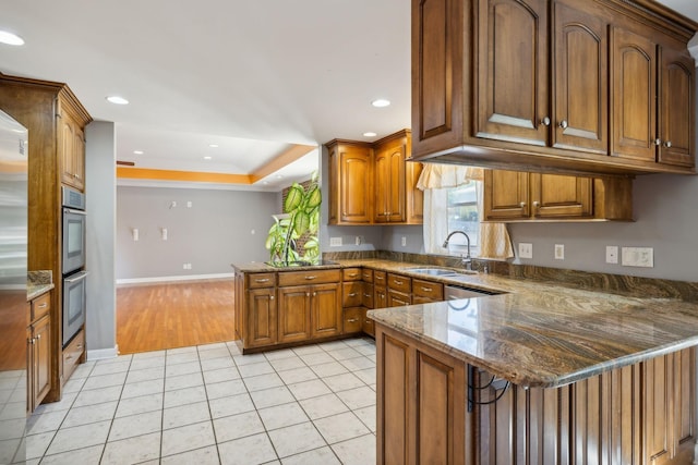 kitchen featuring sink, double oven, kitchen peninsula, dark stone counters, and light tile patterned floors