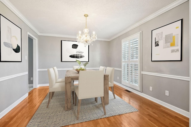 dining room with ornamental molding, wood-type flooring, a textured ceiling, and an inviting chandelier