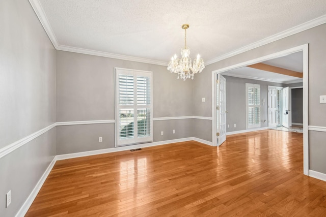 spare room with wood-type flooring, a textured ceiling, an inviting chandelier, and crown molding