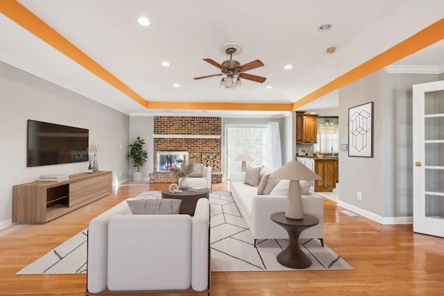 living room with ceiling fan, light hardwood / wood-style floors, ornamental molding, and a brick fireplace