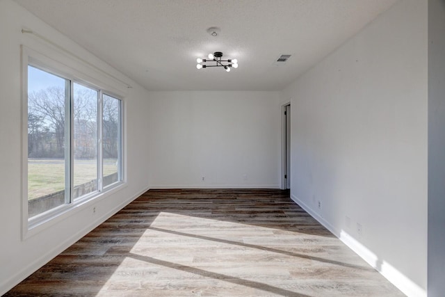 empty room with dark hardwood / wood-style flooring, plenty of natural light, and an inviting chandelier