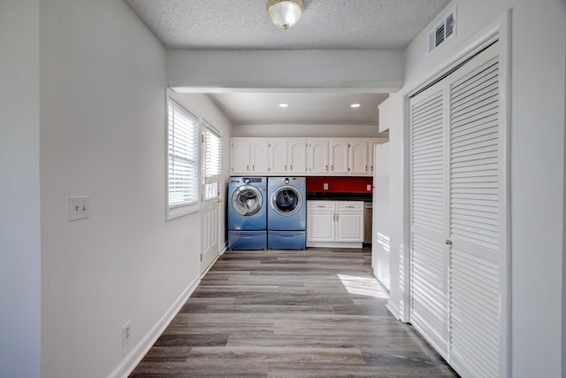 clothes washing area with light hardwood / wood-style floors, cabinets, a textured ceiling, and washing machine and clothes dryer