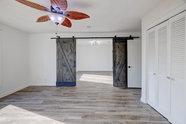 interior space featuring ceiling fan, a barn door, a textured ceiling, a closet, and light wood-type flooring