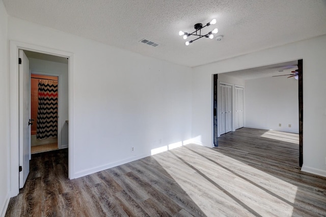 spare room featuring ceiling fan with notable chandelier, a textured ceiling, and dark wood-type flooring