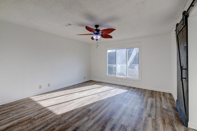 unfurnished room with dark hardwood / wood-style flooring, a barn door, a textured ceiling, and ceiling fan